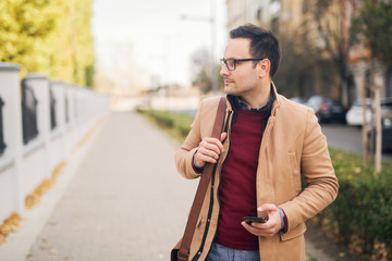 Wall Mural - Businessman with eyeglasses standing on the street holding phone.