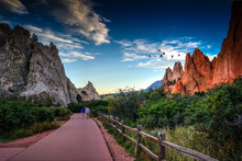 Rear View Of People Walking On Footpath By Rock Formation And Plants Against Sky At Colorado Springs
