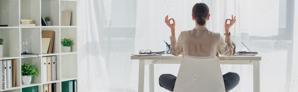 panoramic shot of businesswoman meditating in lotus pose with gyan mudra at workplace with incense stick - obrazy, fototapety, plakaty 