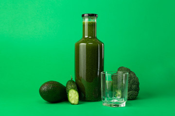 Bottle and empty glass with green natural freshly squeezed vegetable juice smoothie with ingredients isolated on green background. Detox diet is good for low-calorie foods. Healthy eating concept.