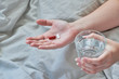 © Forgem - Top view of hands of young woman. Sitting in bed and holding tablets and pills, glass of water.
