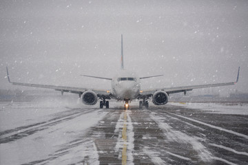 Airliner on runway in blizzard. Aircraft during taxiing during heavy snow. Passenger plane in snow at airport. Passenger airplane taxiing for take off at airport during snow blizzard