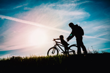 Wall Mural - father help little daughter to ride bike at sunset nature