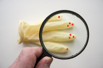 A man's hand holds a magnifying glass through which you can see coronaviruses on rubber gloves