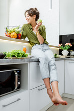 Full Length Portrait Of A Young And Cheerful Woman With Healthy Raw Food On The Kitchen At Home. Vegetarianism, Wellbeing And Healthy Lifestyle Concept