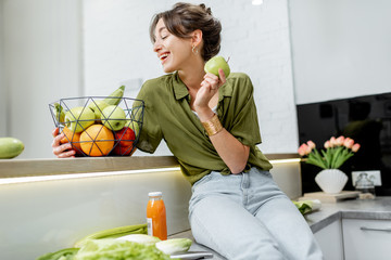 Portrait of a young and cheerful woman with healthy raw food on the kitchen at home. Vegetarianism, wellbeing and healthy lifestyle concept