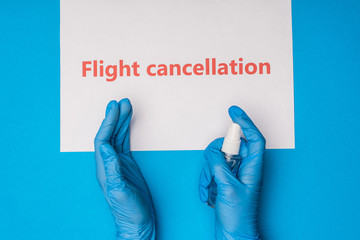 Wall Mural - Top view of doctor holding bottle of hand sanitizer near card with flight cancellation lettering on blue background