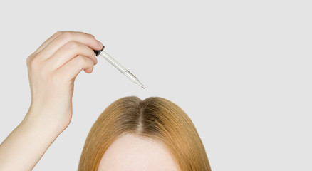 A glass pipette with a hair growth agent is applied to the parting of the hair, red hair. Hair care. Light background, free space for text.