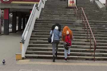 two girls climb up a large wide staircase on a street in a big city.