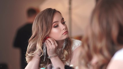 Wall Mural - Beautiful young girl dresses earrings in front of a mirror.