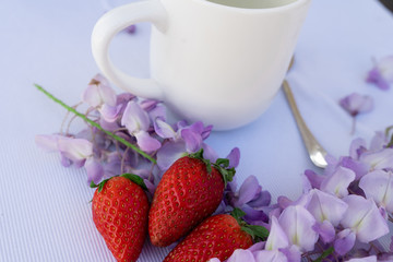 white cup with strawberries and purple flowers  on a table for breakfast