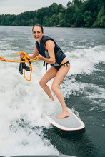 Happy Smiling Woman Wake Boarding Behind Boat On Lake Surrounded By Trees