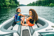 © Inti St. Clair - Smiling happy girls in life jackets on boat on lake surrounded by trees, wind blowing hair