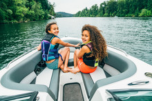 Smiling Happy Girls In Life Jackets On Boat On Lake Surrounded By Trees, Wind Blowing Hair