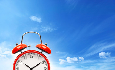 Red alarm clock on blue sky background.