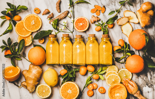Immune boosting vitamin health defending drink. Flat-lay of fresh turmeric, ginger, citrus juice shot in glass bottles over marble background, top view. Vegan Immunity system booster