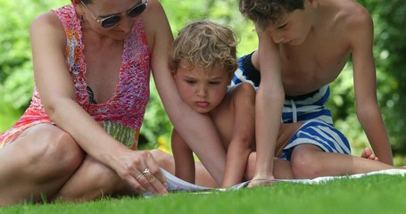 Wall Mural - Children absorbed by story outdoors. Mother reading story book to children. Parent turning page