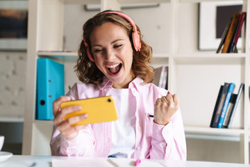 Canvas Print - Photo of excited woman playing game on phone and making winner gesture