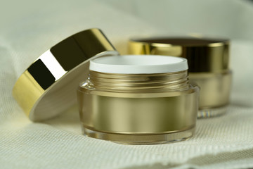 Mockup empty luxury golden two cream jars for skincare and beauty skin on brown fabric folds background.