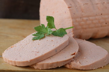 Pink homemade chicken sausage with parsley sliced on wooden cutting board on dark brown background