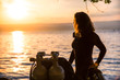 Female Scuba Diving Instructor Wearing a Wet Suit Standing Next to a Twin Tank at Sunset
