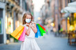 Portrait of adorable little girl in mask walking with shopping bags outdoors in european city.