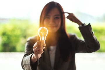 Wall Mural - closeup image of a thinking woman holding and showing glowing light bulb