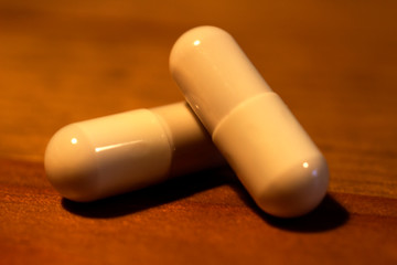 two white pills capsules close up macro on wooden background. antibiotics