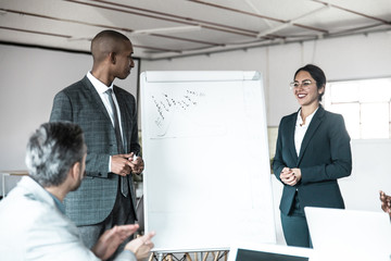 Wall Mural - Cheerful speakers standing near whiteboard during presentation. Employees sitting and applauding colleagues. Business meeting concept