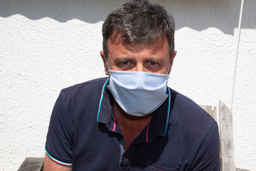 caucasian man standing outdoor in front building home wearing medical protective mask to prevent pandemic disease coronavirus