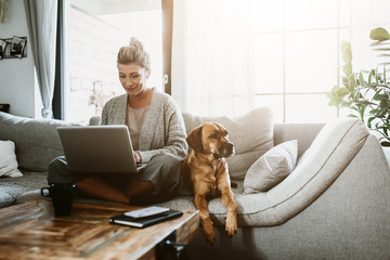 Businesswoman working on laptop computer sitting at home with a dog pet and managing her business via home office during Coronavirus or Covid-19 quarantine