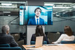 © Mangostar - Employees listening to young leader during video conference. Business people looking at monitor screen during video conference in office. Business conference concept
