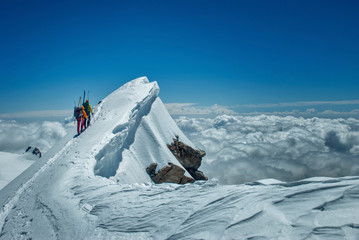 Two guys ski mountaineeres go to the top along a fantastic ridge with a snow cornice. Sea of clouds below tht summit to the horizon