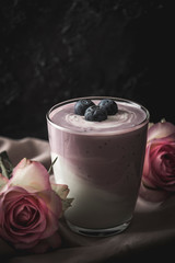 Glass with blueberry yogurt decorated with roses on dark background