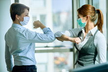 Female Colleagues With Face Masks Elbow Bumping While Greeting In The Office.