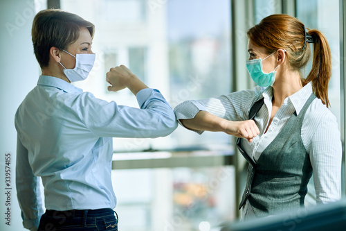 Female colleagues with face masks elbow bumping while greeting in the office Tableau sur Toile