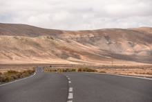An Empty Road On Fuerteventura Countryside, With Volcanic Mountains In The Background