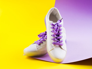 Wall Mural - White sneakers with purple laces on yellow and purple split background. Modern minimal fashion art trendy bold color still life