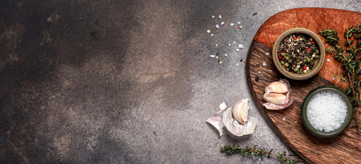 Food background on a dark concrete table. Spices, herbs and knife on a wooden cutting board, top view, flat lay. Free space for text. Ingredients for cooking on a dark background, copy space.