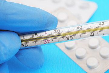 hand in medical gloves holding mercury thermometer showing fever temperature