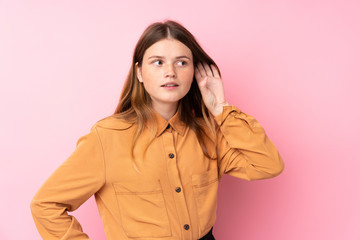 Ukrainian teenager girl over isolated pink background listening to something by putting hand on the ear