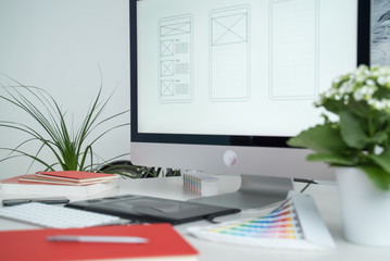 Web designer at work. Graphic designer. Mobile application design. Designer desktop. UX, UI design. Thumbnails of a mobile application on a computer screen. Gadgets, sketchbook and phone on the table