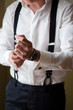 © WellStock - Groom's morning. A man in a white shirt and suspenders puts a watch on his wrist. Close up, no face. Preparation for the wedding