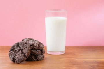 Glass of fresh milk with crunchy baked chocolate sugar cookies on wooden table with pink background. Ideas of school breakfast or fast snack for students.