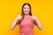 Young redhead woman over isolated yellow background giving a thumbs up gesture