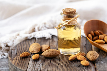 Concept of organic vegetable oils for cooking and cosmetology. Almond nuts to illustrate ingredients. Rustic wooden background, natural oil in glass bottles. Close up, macro