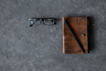 Brown craft leather notebook, pen and glasses on gray background