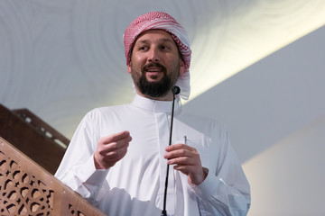 Canvas Print - Muslims young arabic Imam has a speech on friday afternoon prayer in mosque. Muslims have gathered for the friday afternoon prayer in mosque and are listening to the speech of imam