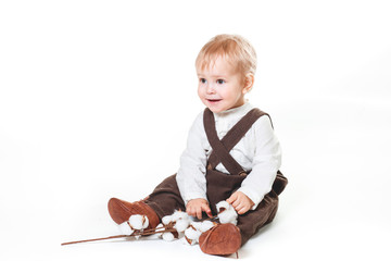 A cute stylish one year old boy in a white linen shirt and brown trousers looks a smile