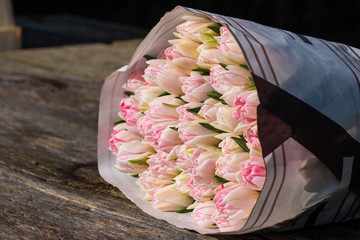 a beautiful bouquet of pink tulips on dark wooden surface in sunny day. Background for Valentins or international woman's day. Copy space